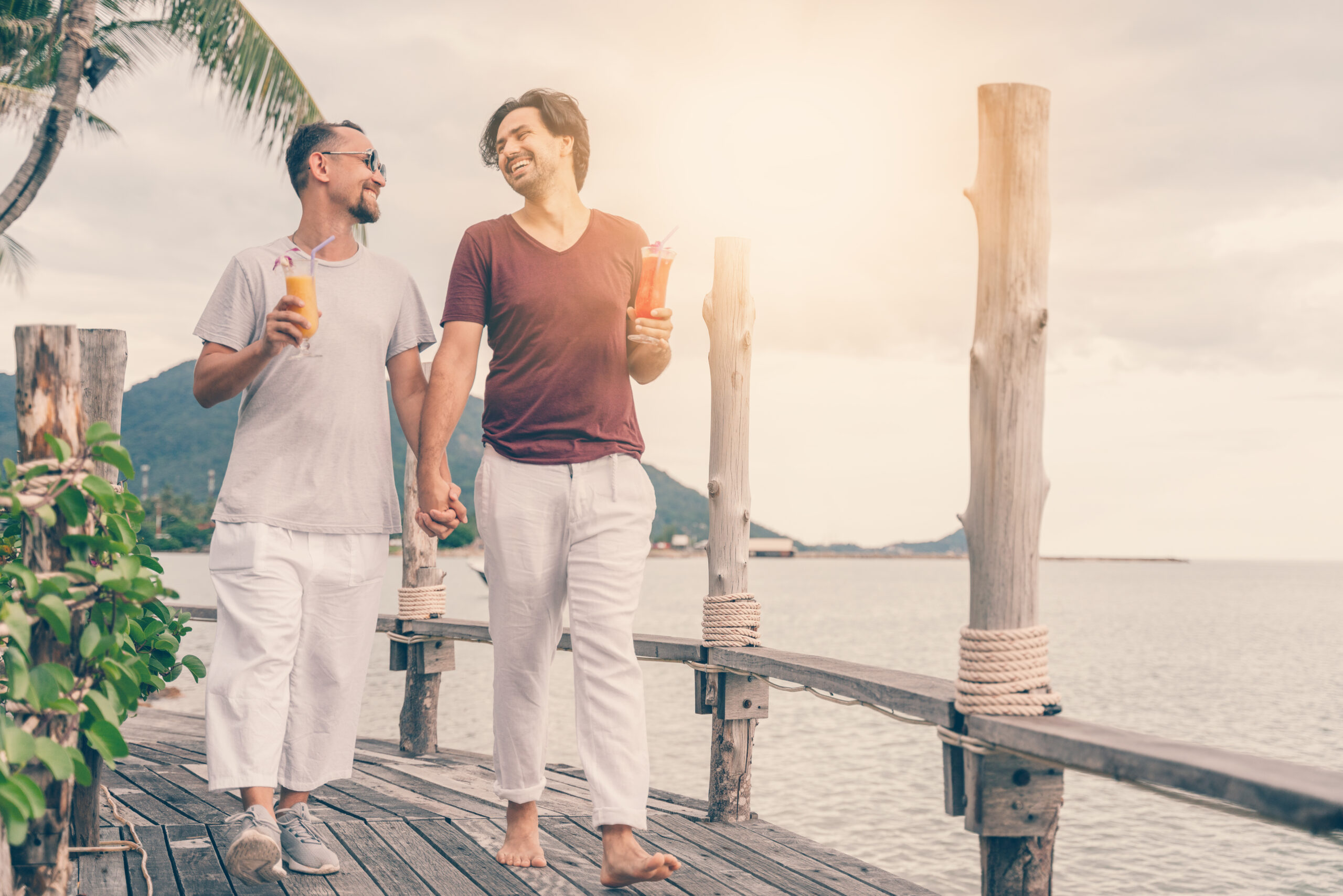 Happy handsome young men, gay family in a tropical resort with fruit necks, LGBT values, equal rights for everyone. Vacations and Travel.